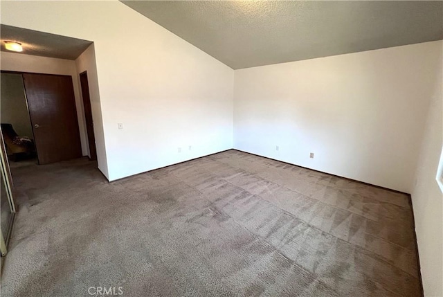 carpeted spare room featuring a textured ceiling and lofted ceiling