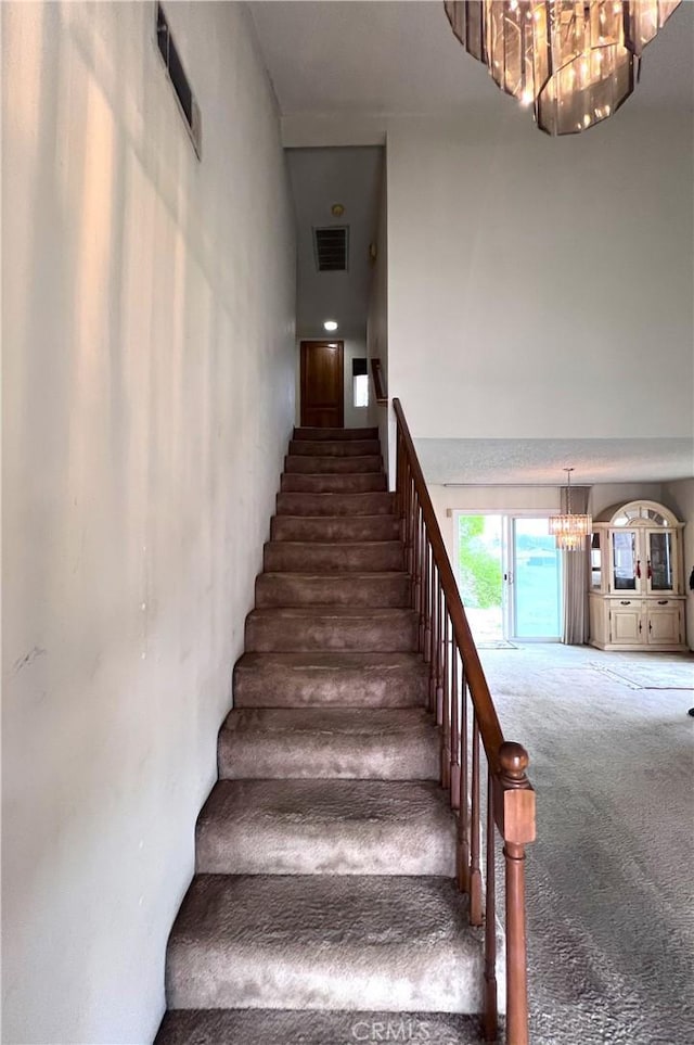 stairs with carpet floors and a notable chandelier