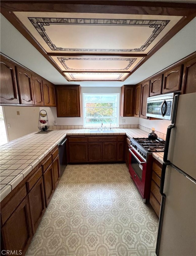 kitchen featuring tile counters, sink, dark brown cabinets, and stainless steel appliances