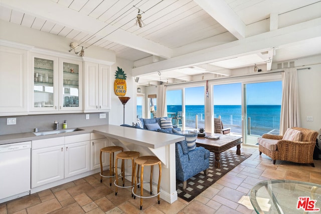 kitchen with beamed ceiling, white dishwasher, sink, white cabinetry, and a water view