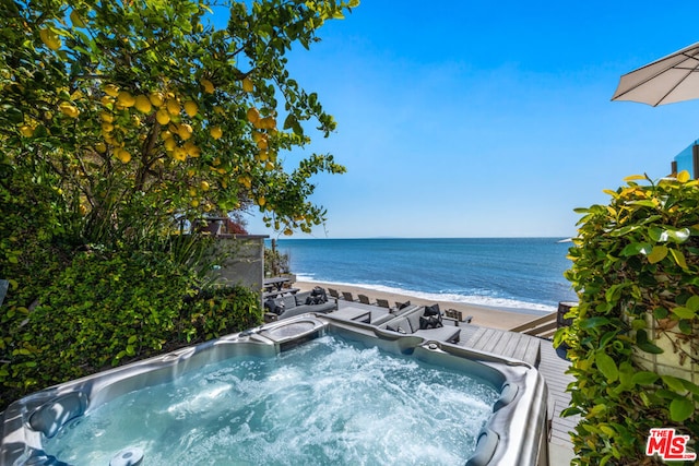 view of swimming pool with a hot tub, a deck with water view, and a beach view