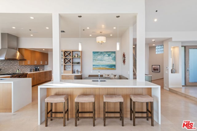 kitchen featuring decorative backsplash, wall chimney exhaust hood, a breakfast bar area, hanging light fixtures, and a large island