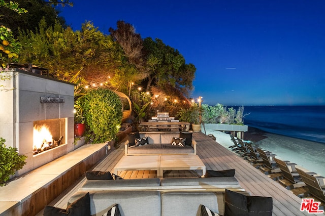 patio at twilight with a deck with water view and an outdoor fireplace