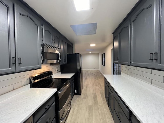 kitchen featuring a skylight, light hardwood / wood-style flooring, stainless steel appliances, and tasteful backsplash