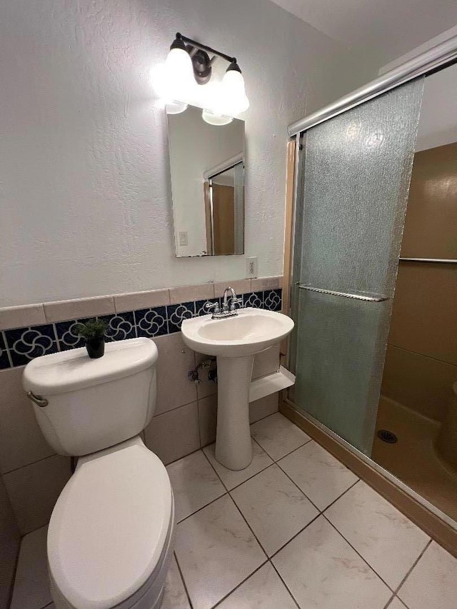 bathroom featuring tile patterned floors, toilet, tile walls, and a shower with shower door