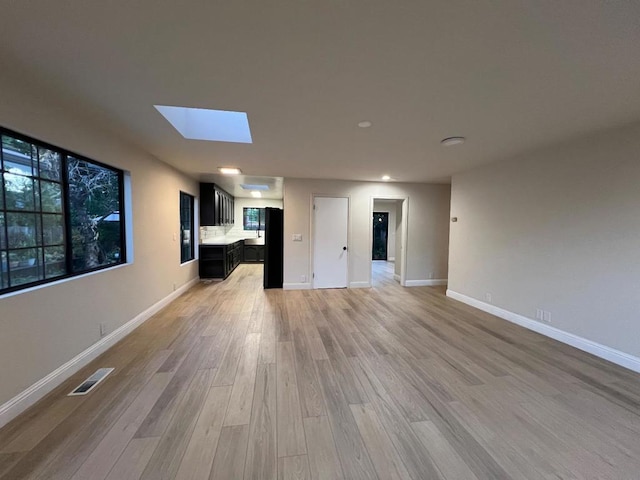 unfurnished living room featuring light wood-type flooring and a skylight