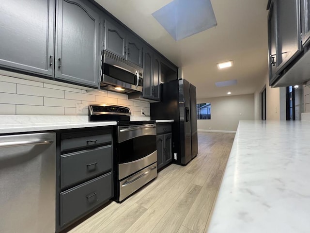 kitchen featuring light hardwood / wood-style floors, decorative backsplash, a skylight, and appliances with stainless steel finishes