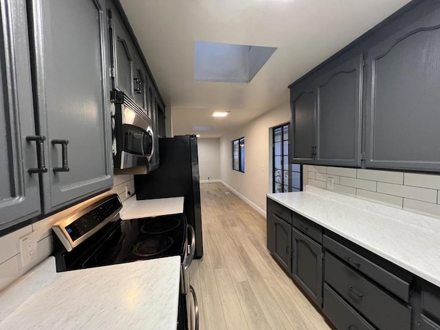 kitchen with a skylight, stove, decorative backsplash, light hardwood / wood-style flooring, and black fridge