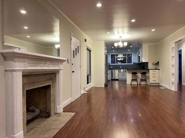 living room featuring crown molding, sink, dark wood-type flooring, a tile fireplace, and a chandelier