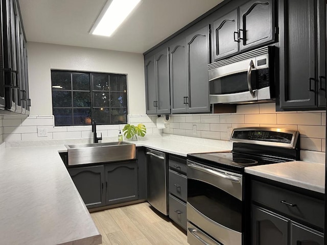 kitchen featuring decorative backsplash, sink, stainless steel appliances, and light wood-type flooring