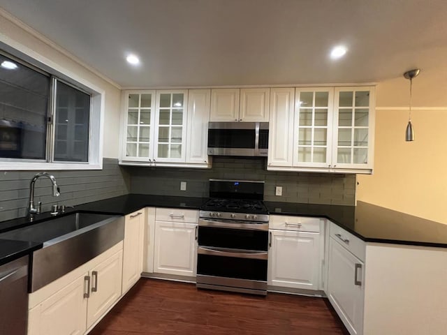 kitchen featuring appliances with stainless steel finishes, white cabinets, decorative light fixtures, sink, and backsplash