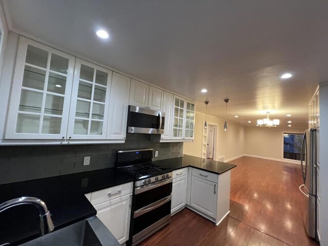 kitchen with pendant lighting, appliances with stainless steel finishes, sink, white cabinets, and an inviting chandelier