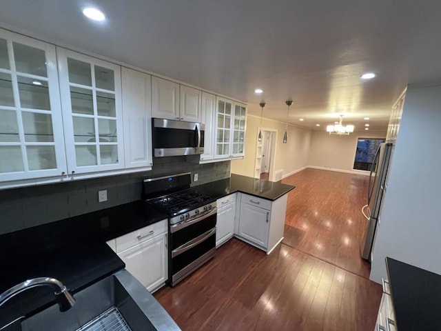 kitchen featuring white cabinets, stainless steel appliances, decorative backsplash, hanging light fixtures, and a notable chandelier