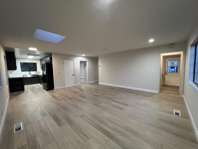 unfurnished living room featuring sink, a skylight, and light hardwood / wood-style floors