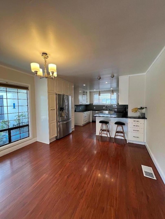 kitchen with a kitchen breakfast bar, stainless steel refrigerator with ice dispenser, decorative light fixtures, white cabinets, and a chandelier