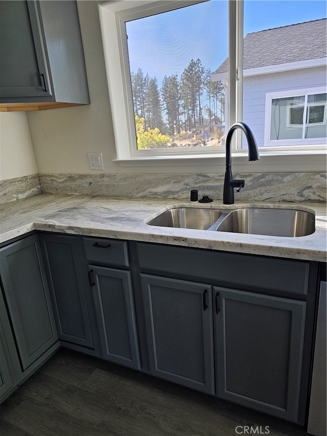 kitchen with light stone counters, dishwasher, dark wood-type flooring, gray cabinets, and sink