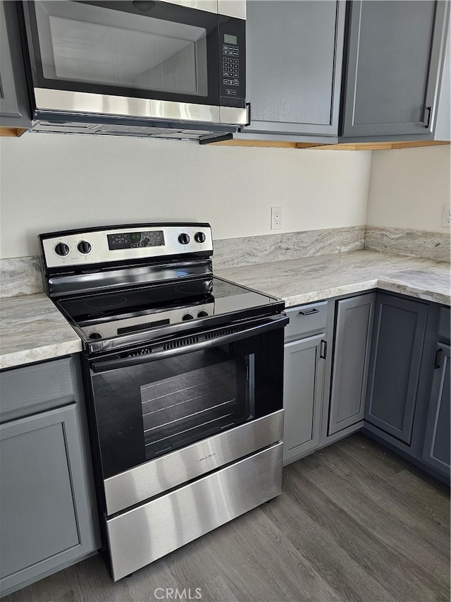 kitchen with light stone countertops, appliances with stainless steel finishes, gray cabinetry, and dark hardwood / wood-style flooring