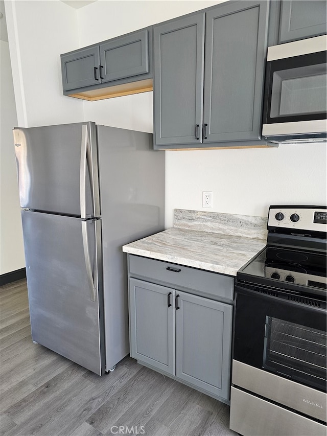 kitchen with appliances with stainless steel finishes, gray cabinets, and light wood-type flooring