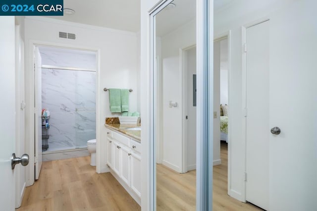 bathroom featuring toilet, tiled shower, wood-type flooring, and vanity