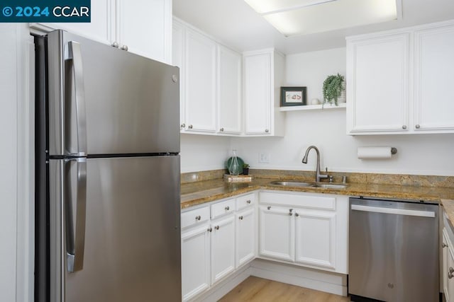 kitchen featuring light hardwood / wood-style floors, appliances with stainless steel finishes, dark stone counters, white cabinets, and sink