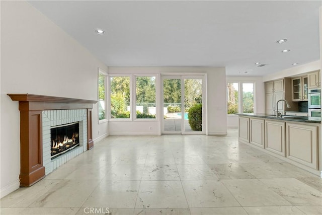 unfurnished living room featuring a brick fireplace, baseboards, a sink, and recessed lighting