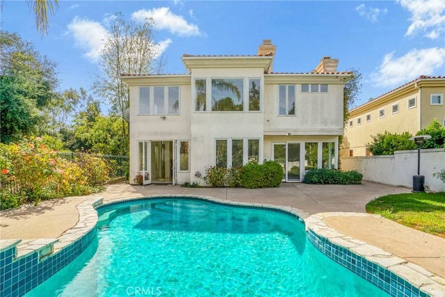 rear view of house with a chimney, a patio area, a fenced in pool, and stucco siding