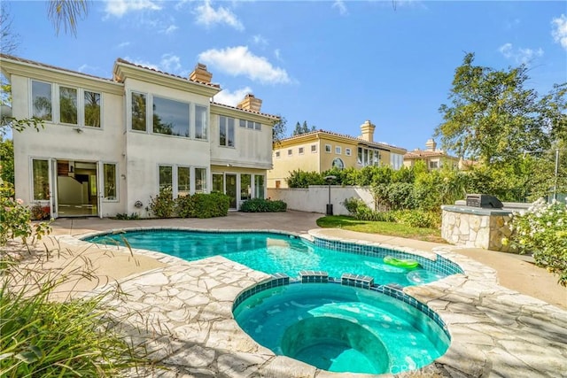 view of swimming pool with a patio, an outdoor kitchen, fence, and a pool with connected hot tub