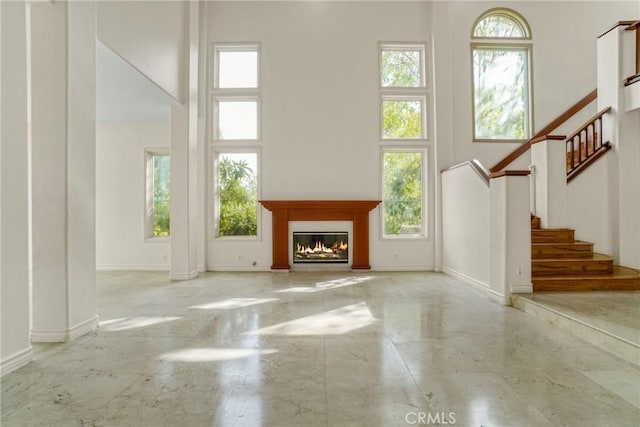 unfurnished living room featuring a towering ceiling, baseboards, stairway, and a glass covered fireplace