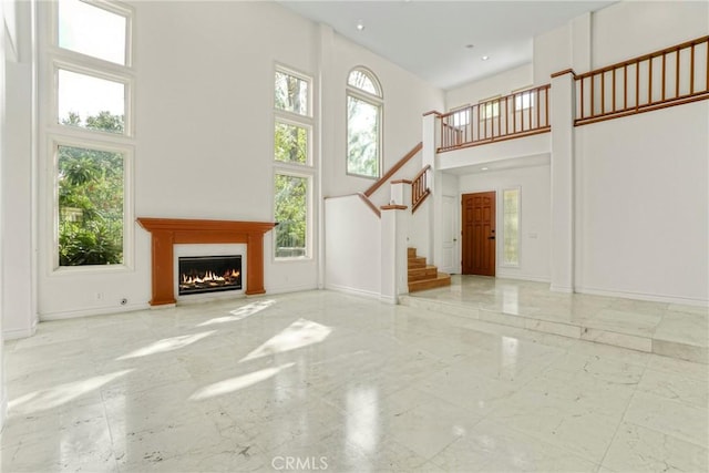 unfurnished living room featuring stairs, a high ceiling, baseboards, and a wealth of natural light