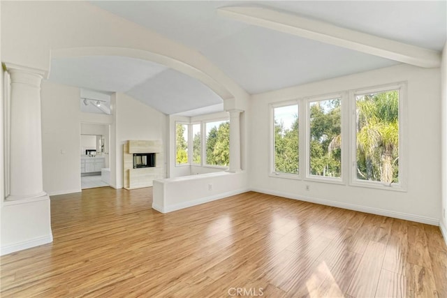 unfurnished living room with lofted ceiling with beams, light wood-style flooring, a premium fireplace, baseboards, and ornate columns