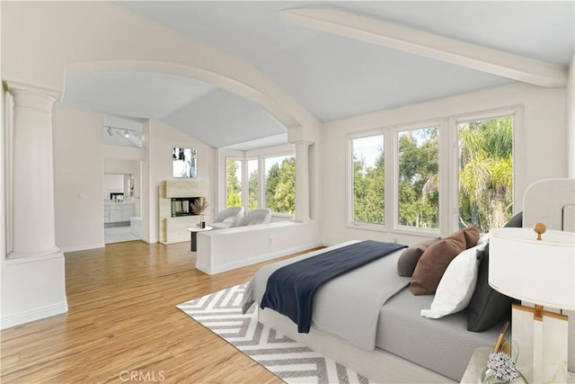 bedroom with arched walkways, lofted ceiling with beams, light wood-type flooring, ornate columns, and a multi sided fireplace