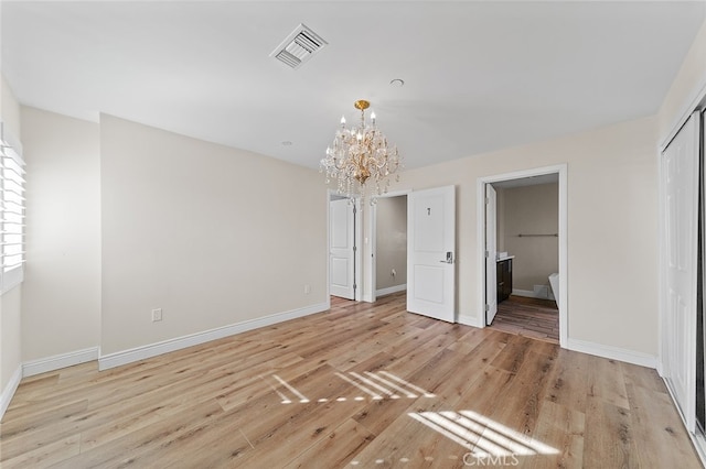 unfurnished bedroom with connected bathroom, a closet, a notable chandelier, and light hardwood / wood-style floors