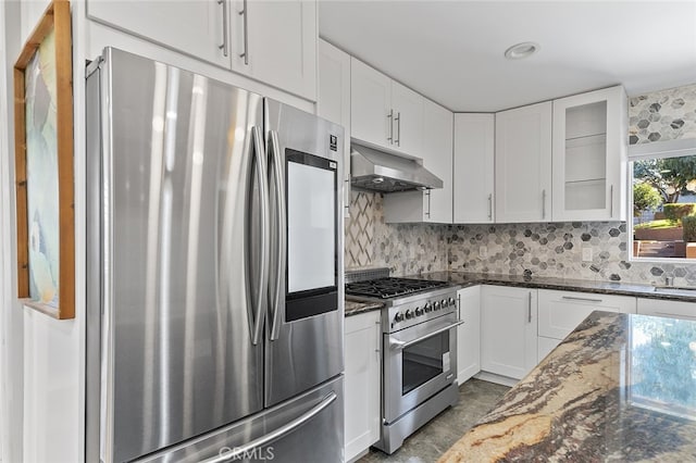 kitchen featuring appliances with stainless steel finishes, white cabinetry, dark stone counters, and backsplash