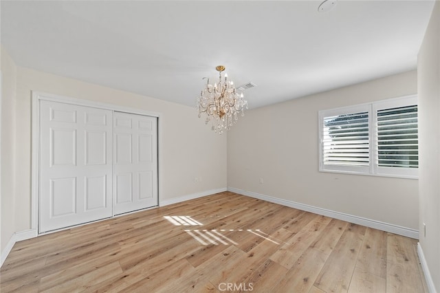 unfurnished bedroom with an inviting chandelier, light wood-type flooring, and a closet