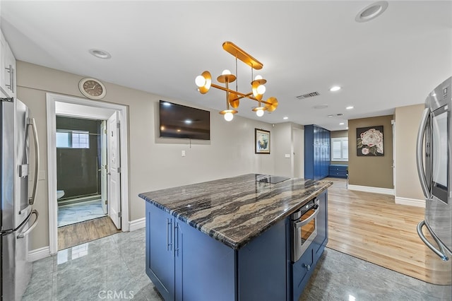 kitchen with appliances with stainless steel finishes, hanging light fixtures, dark stone counters, and light hardwood / wood-style floors