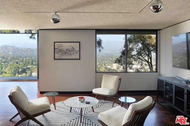 sitting room with plenty of natural light, a wall of windows, a textured ceiling, and dark wood-type flooring