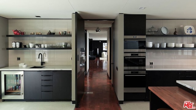 kitchen featuring sink, stainless steel double oven, beverage cooler, tasteful backsplash, and hardwood / wood-style floors