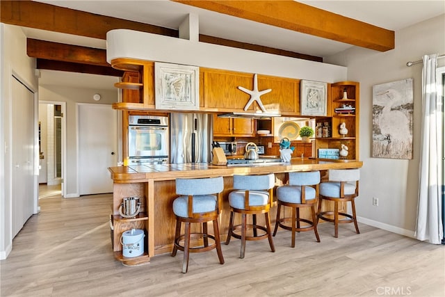 kitchen with a kitchen breakfast bar, kitchen peninsula, beamed ceiling, and light wood-type flooring