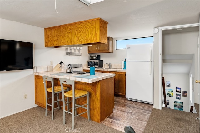 kitchen with kitchen peninsula, tile countertops, wood-type flooring, white fridge, and sink