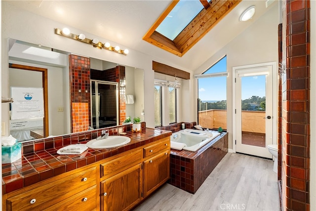 full bathroom featuring shower with separate bathtub, hardwood / wood-style flooring, toilet, vaulted ceiling with skylight, and vanity