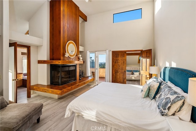 bedroom with a large fireplace, high vaulted ceiling, and light hardwood / wood-style flooring