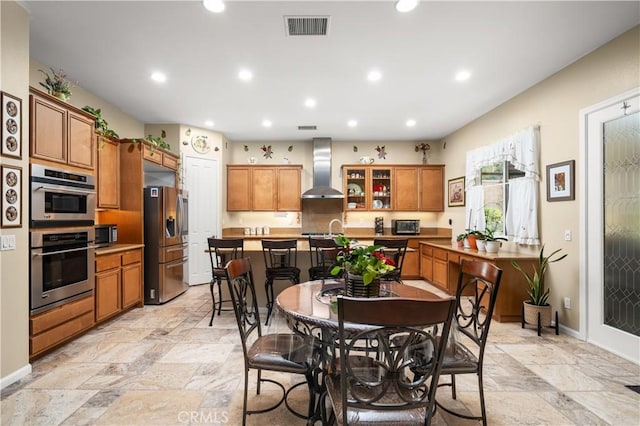 kitchen with a center island with sink, stainless steel appliances, wall chimney range hood, and sink