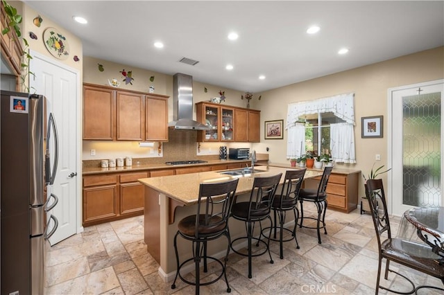 kitchen with sink, stainless steel appliances, wall chimney range hood, a kitchen bar, and a kitchen island with sink