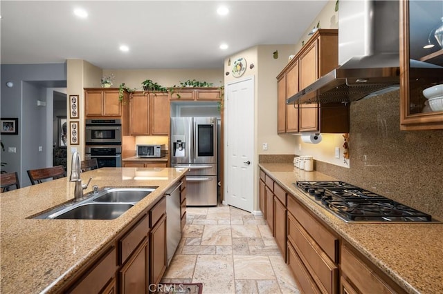 kitchen with decorative backsplash, light stone counters, stainless steel appliances, sink, and wall chimney range hood