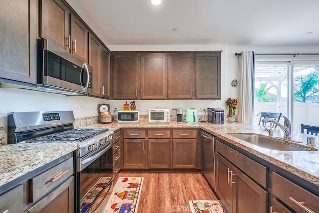 kitchen with light stone countertops, appliances with stainless steel finishes, sink, dark brown cabinets, and light hardwood / wood-style floors