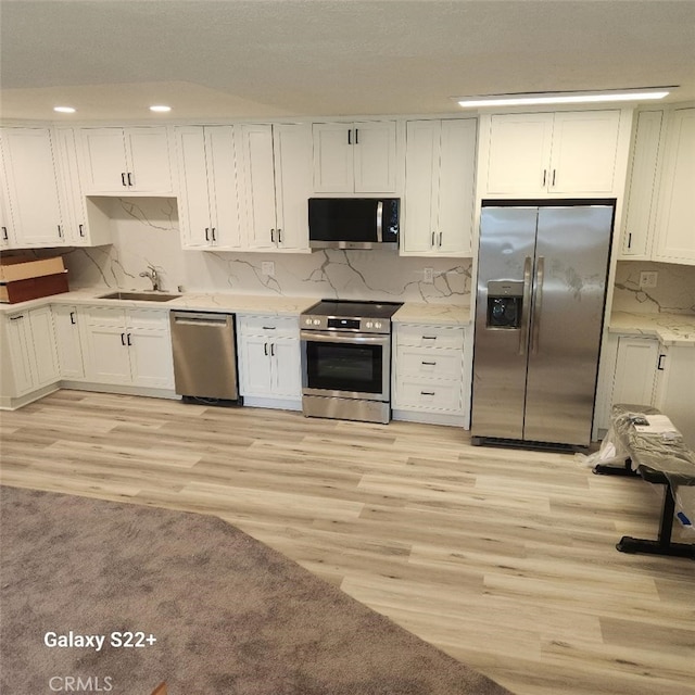 kitchen with white cabinetry, sink, stainless steel appliances, and light hardwood / wood-style floors