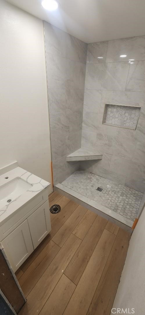 bathroom with tiled shower, vanity, and wood finished floors