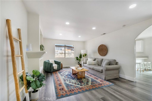 living room featuring arched walkways, wood finished floors, visible vents, and baseboards