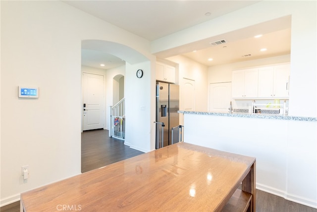 kitchen featuring dark hardwood / wood-style floors, kitchen peninsula, stainless steel fridge with ice dispenser, white cabinetry, and light stone counters