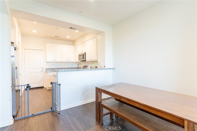 kitchen featuring kitchen peninsula, stainless steel appliances, white cabinets, light stone counters, and dark hardwood / wood-style flooring